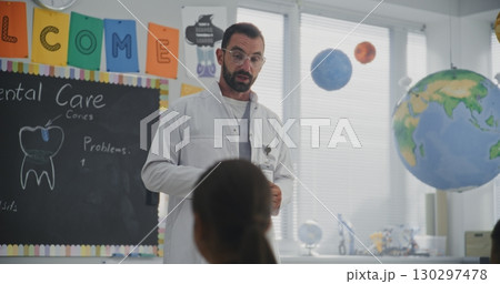 Doctor Visiting Classroom, Giving Lecture to Curious Primary School Students About Dental Care and Hygiene Doctor Visiting Classroom, Giving Lecture to Curious Primary School Students About Dental Care and Hygiene 130297478