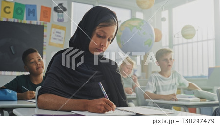 Muslim Primary School Girl Wearing Hijab Writing School Test in Notebook, Studying in Multicultural Classroom Muslim Primary School Girl Wearing Hijab Writing School Test in Notebook, Studying in Multicultural Classroom 130297479