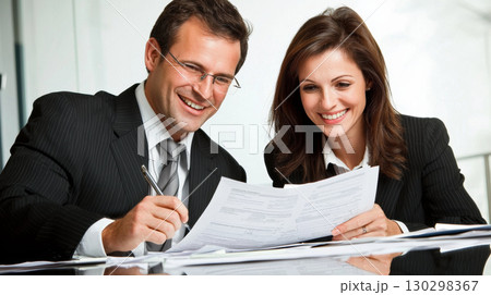man and woman business attire are smiling while reviewing documents together modern office setting. Their expressions convey man and woman business attire are smiling while reviewing documents together modern office setting. Their expressions convey 130298367