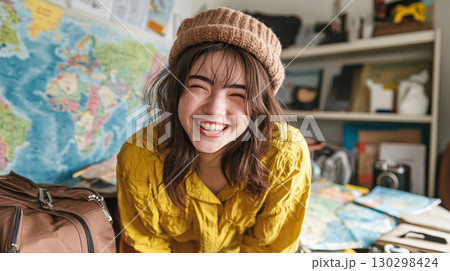 cheerful young woman in yellow shirt and brown hat smiles brightly in cozy room filled with maps and travel items cheerful young woman in yellow shirt and brown hat smiles brightly in cozy room filled with maps and travel items 130298424