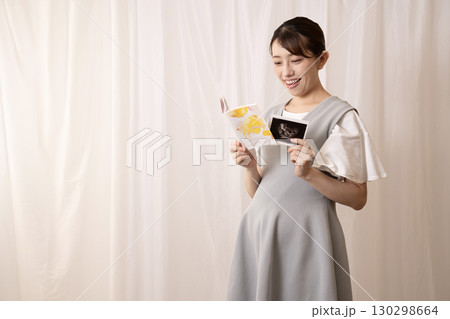母子手帳とエコー写真を見る妊婦の女性 母子手帳とエコー写真を見る妊婦の女性 130298664
