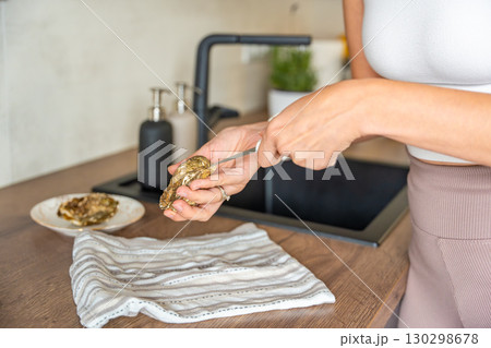 Female hands struggling to open a fresh oyster at home with a special oyster knife. Risks and challenges of handling shellfish without professional training Female hands struggling to open a fresh oyster at home with a special oyster knife. Risks and challenges of handling shellfish without professional training 130298678