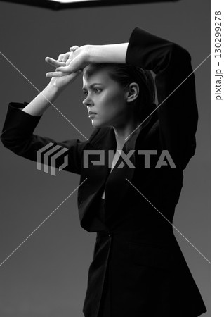 Black and white portrait of a serious woman in a blazer with raised arms expressing emotion and intensity. 130299278