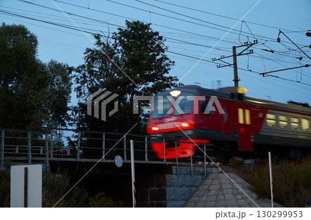 A Red Electric Train Crossing at Dusk, creating a dynamic scene of urban movement amidst twilight 130299953