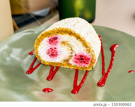 Raspberry cream Swiss roll dessert on a green plate. Confectionery treat with fruit filling and powdered sponge exterior. 130300062