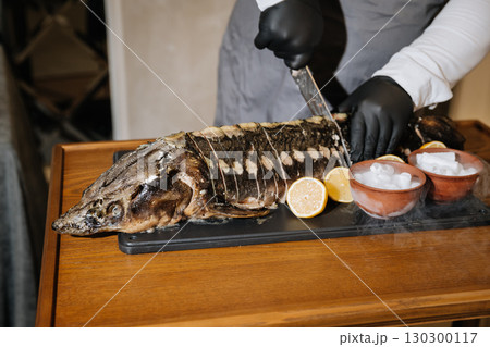 Chef slicing baked sturgeon with lemon and dry ice for elegant gourmet presentation 130300117
