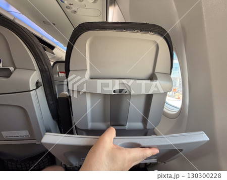 Passenger unfolding tray table on airplane seat. Practicality, space management, and in-flight comfort during air travel. Passenger unfolding tray table on airplane seat. Practicality, space management, and in-flight comfort during air travel. 130300228