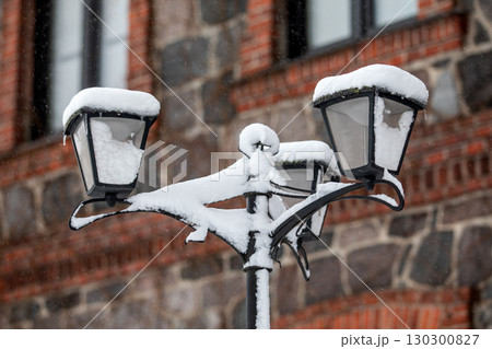 Vintage Street Lamp Covered in Snow During Winter Storm Near Brick Stone Building 130300827