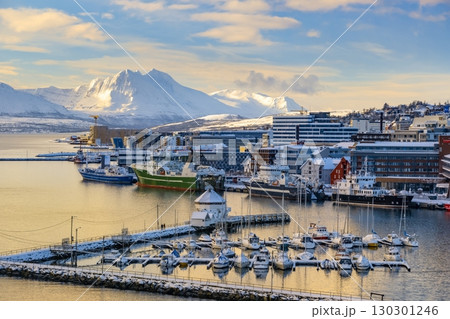 Snow-covered Troms harbor with docked boats and ships, nestled against a backdrop of snow-capped mountains and colorful buildings. A serene winter scene capturing the essence of Norwegian coastal life Snow-covered Troms harbor with docked boats and ships, nestled against a backdrop of snow-capped mountains and colorful buildings. A serene winter scene capturing the essence of Norwegian coastal life 130301246