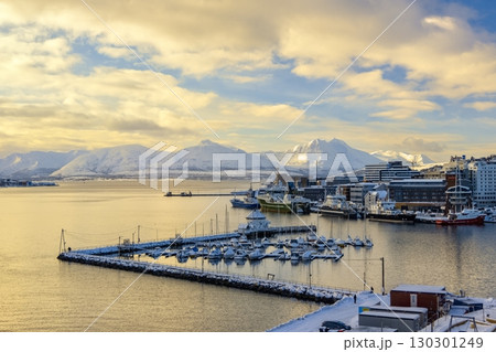 Snow-covered Troms harbor with docked boats and ships, nestled against a backdrop of snow-capped mountains and colorful buildings. A serene winter scene capturing the essence of Norwegian coastal life Snow-covered Troms harbor with docked boats and ships, nestled against a backdrop of snow-capped mountains and colorful buildings. A serene winter scene capturing the essence of Norwegian coastal life 130301249