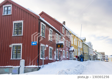 Vibrant traditional wooden houses in Troms, Norway display vivid colors against a snowy winter backdrop. Snow-covered streets enhance the charm of this picturesque Scandinavian town 130301256