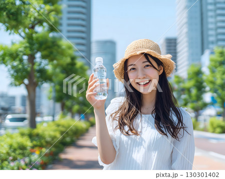 青空の街中で笑顔の日本人女性が水分補給する夏の日常シーン 130301402