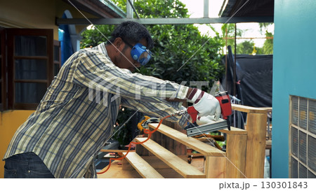 Carpenter securing wooden staircase steps with nail gun while wearing safety goggles and gloves Carpenter securing wooden staircase steps with nail gun while wearing safety goggles and gloves 130301843