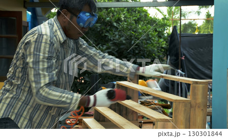 Carpenter fastening wooden staircase steps with pneumatic nail gun while wearing protective gloves and safety goggles Carpenter fastening wooden staircase steps with pneumatic nail gun while wearing protective gloves and safety goggles 130301844