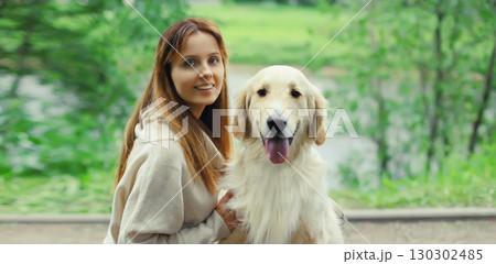 Happy smiling owner woman with Golden Retriever dog sitting together on bench in summer park 130302485