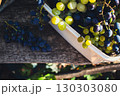 Heap of ripe grape in white basket on wooden bench. Autumn harvest. Autumn fruits. Bunch of juicy black and white grape in sunlight. Autumn agriculture. September nature. Healthy organic grapes.  130303080