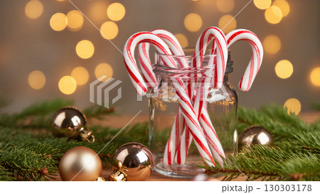 Christmas candy canes in glass jar with fir branches and ornaments, glowing festive lights in background, sweet holiday decor Christmas candy canes in glass jar with fir branches and ornaments, glowing festive lights in background, sweet holiday decor 130303178