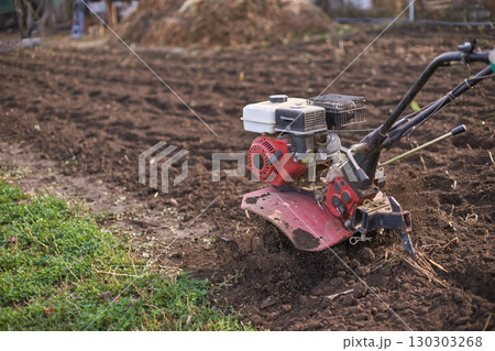 Farming equipment tilling soil in a rural field with red cultivator and green 130303268