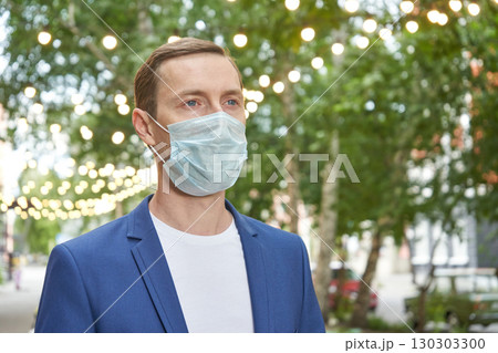 Caucasian male adult wearing face mask outdoors in urban park setting 130303300