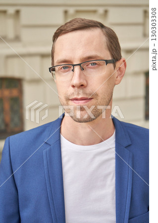 Young caucasian male adult in blue jacket and glasses standing outside building 130303308