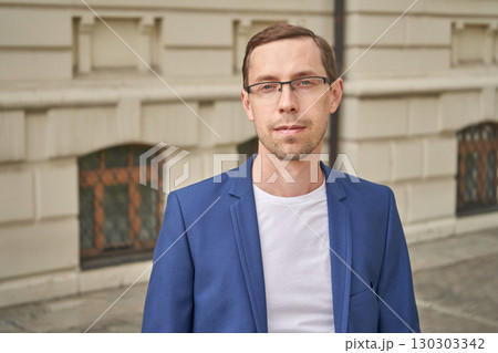 Caucasian young adult male in blue blazer standing outside historical building 130303342