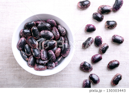 Dried scarlet runner beans in a white bowl on linen. Raw and large seeds of purple colored speckled runner beans, a variety of Phaseolus coccineus, also known as multiflora bean, butter, or fire bean. Dried scarlet runner beans in a white bowl on linen. Raw and large seeds of purple colored speckled runner beans, a variety of Phaseolus coccineus, also known as multiflora bean, butter, or fire bean. 130303443