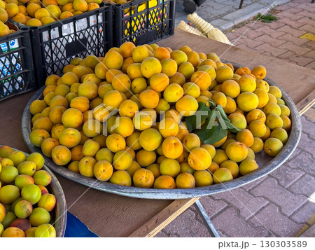 Apricots displayed in metal tray with green leaves at market. Agriculture, farming and seasonal fruit harvest with natural lifestyle and nutrition. Apricots displayed in metal tray with green leaves at market. Agriculture, farming and seasonal fruit harvest with natural lifestyle and nutrition. 130303589