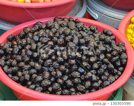 Close-up of shiny black olives in plastic bucket on market stall. Agriculture, farming, and seasonal fruit harvest with nutrition and healthy lifestyle. 130303590