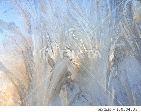 Frost patterns create intricate designs on a window in the early morning light 130304535