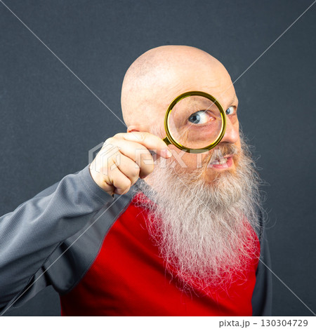 Elderly man examining his surroundings with a magnifying glass after sunset indoors 130304729
