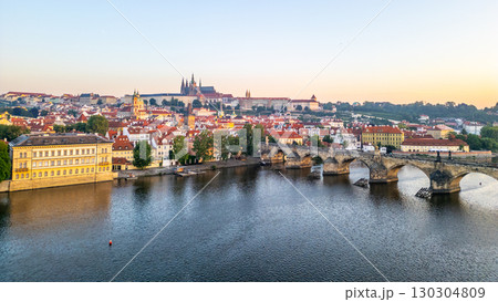 Bright colors fill the sky as the sun rises over Prague, illuminating the Vltava River and its medieval architecture. 130304809
