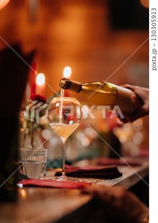 Hand pouring white wine into glass at festive dinner table with candlelight and decor Hand pouring white wine into glass at festive dinner table with candlelight and decor 130305913