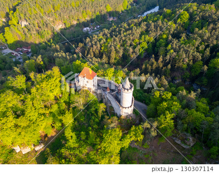 Golden sunlight bathes Kokorin Castle during a serene evening in Czechia. The aerial view showcases its medieval architecture surrounded by lush greenery and the winding landscape. 130307114