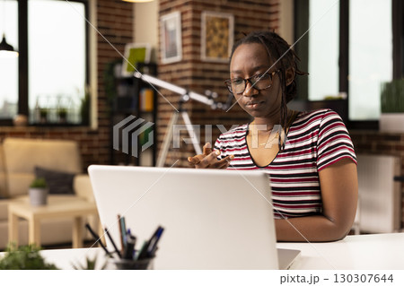Focused black woman speaking with team during virtual meeting on laptop. African american female employee working from home, participating in video conference with coworkers on personal computer. 130307644