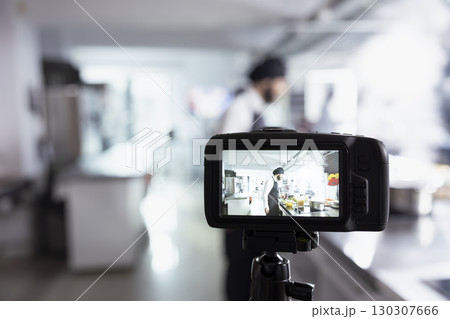 Professional chef mentors his audience through a video on the tripod camera, explaining preparation methods and plating techniques. Virtual classroom for online culinary training. Professional chef mentors his audience through a video on the tripod camera, explaining preparation methods and plating techniques. Virtual classroom for online culinary training. 130307666