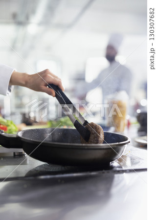 Female chef preparing a juicy beef steak piece for a gourmet meal on the stove, flipping the raw meat with tongs in the pan. Culinary expert preparing a fillet in oil, gastronomy. Close up. Female chef preparing a juicy beef steak piece for a gourmet meal on the stove, flipping the raw meat with tongs in the pan. Culinary expert preparing a fillet in oil, gastronomy. Close up. 130307682