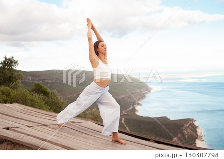 Young woman practicing Warrior Pose yoga on wooden Young woman practicing Warrior Pose yoga on wooden 130307798
