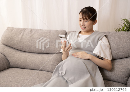 ソファーに座ってスマホを持つ妊娠8ヶ月の女性 130312763