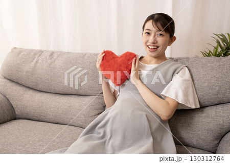 ソファーに座って赤いハートを持つ妊娠8ヶ月の女性 130312764