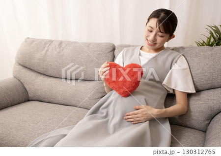 ソファーに座って赤いハートを持つ妊娠8ヶ月の女性 ソファーに座って赤いハートを持つ妊娠8ヶ月の女性 130312765