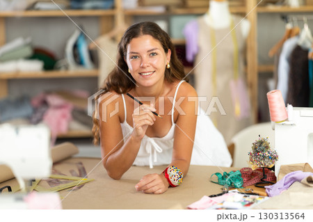 young dressmaker draws a sketch with the help of curved rulers 130313564