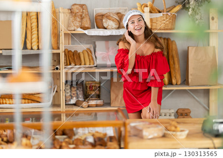 Smiling happy girl in red dress behind bakery counter Smiling happy girl in red dress behind bakery counter 130313565