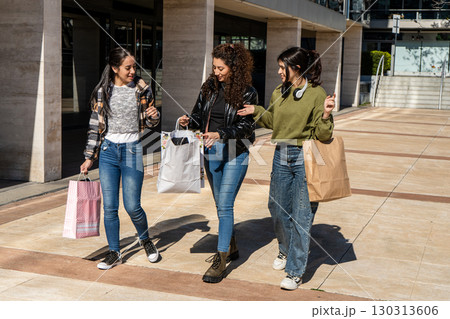 Three young women walking and talking after shopping spree 130313606