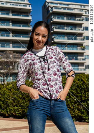 Young latin woman posing with hands in pockets in urban setting 130313614