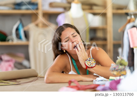 Exhausted young seamstress yawning at worktable Exhausted young seamstress yawning at worktable 130313700