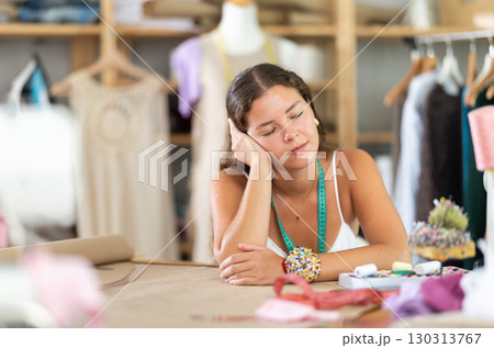 Tired female fashion designer sleeping at worktable in sewing studio Tired female fashion designer sleeping at worktable in sewing studio 130313767