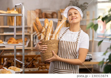Asian woman bakery worker sells baguettes, stands at counter and waits for visitors Asian woman bakery worker sells baguettes, stands at counter and waits for visitors 130313874