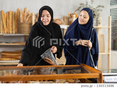 Two girls in traditional Muslim clothing chat and choose delicious bread and croissants together at bakery 130313896