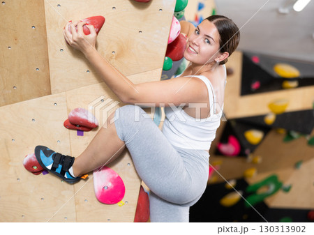 Young female alpinist practicing indoor a rock-climbing on a artificial boulder without safety belts Young female alpinist practicing indoor a rock-climbing on a artificial boulder without safety belts 130313902