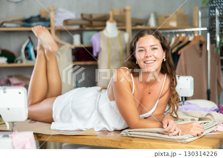 Female dressmaker lying playfully on table in workshop Female dressmaker lying playfully on table in workshop 130314226